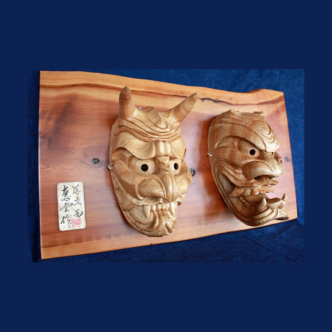 A pair of hand-carved camphor furyu oni masks by Sugicho of Kashima, Saga, mounted on a cedar board
