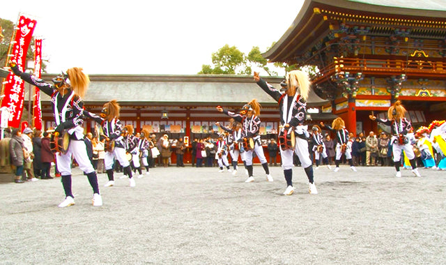 Men-buryu performed on the gravel forecourt of a vermilion shrine before a crowd