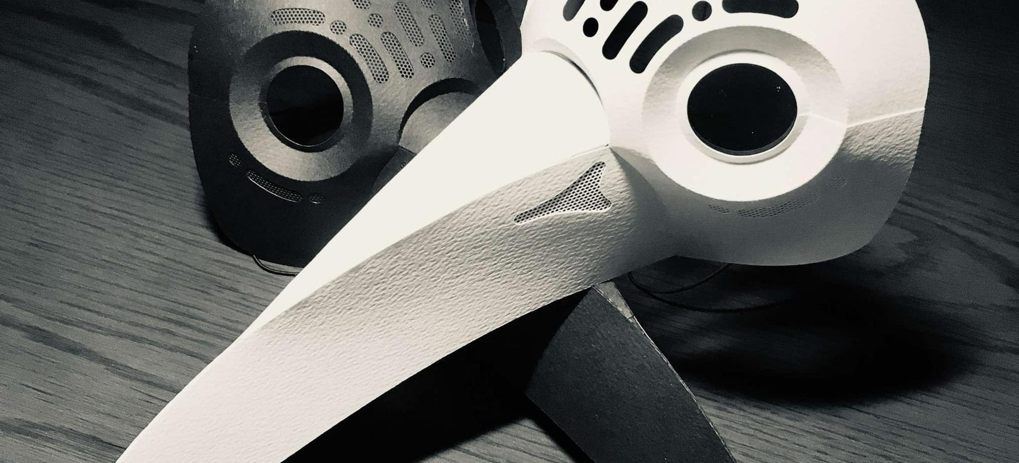 Plague doctor papercraft masks in white and black on dark wood